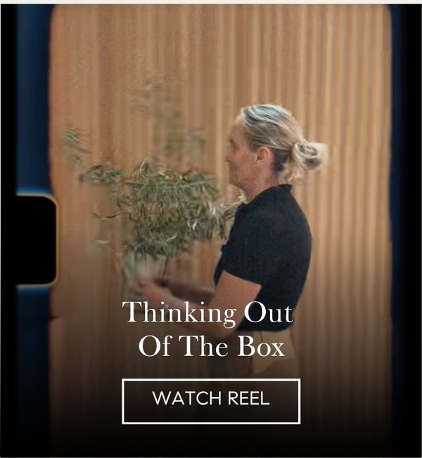 Reel still of a woman carrying an olive branch past a warm wood-slat wall, 'Thinking Out Of The Box' with a Watch Reel button